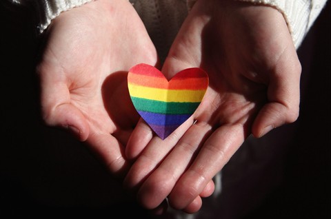 Someone holding out a rainbow heart in their hand.