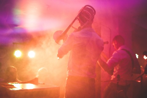 Smoky shot of musicians playing in pink and yellow light on a stage.