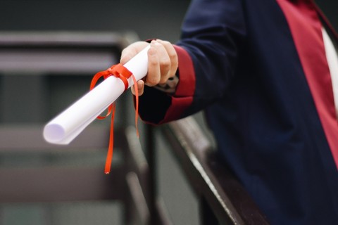 Person holding out a diploma rolled up and tied with a red ribbon.